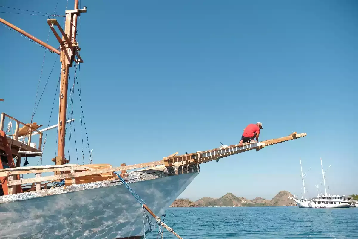 Bowsprit of a wooden phinisi under way, islands on the horizon